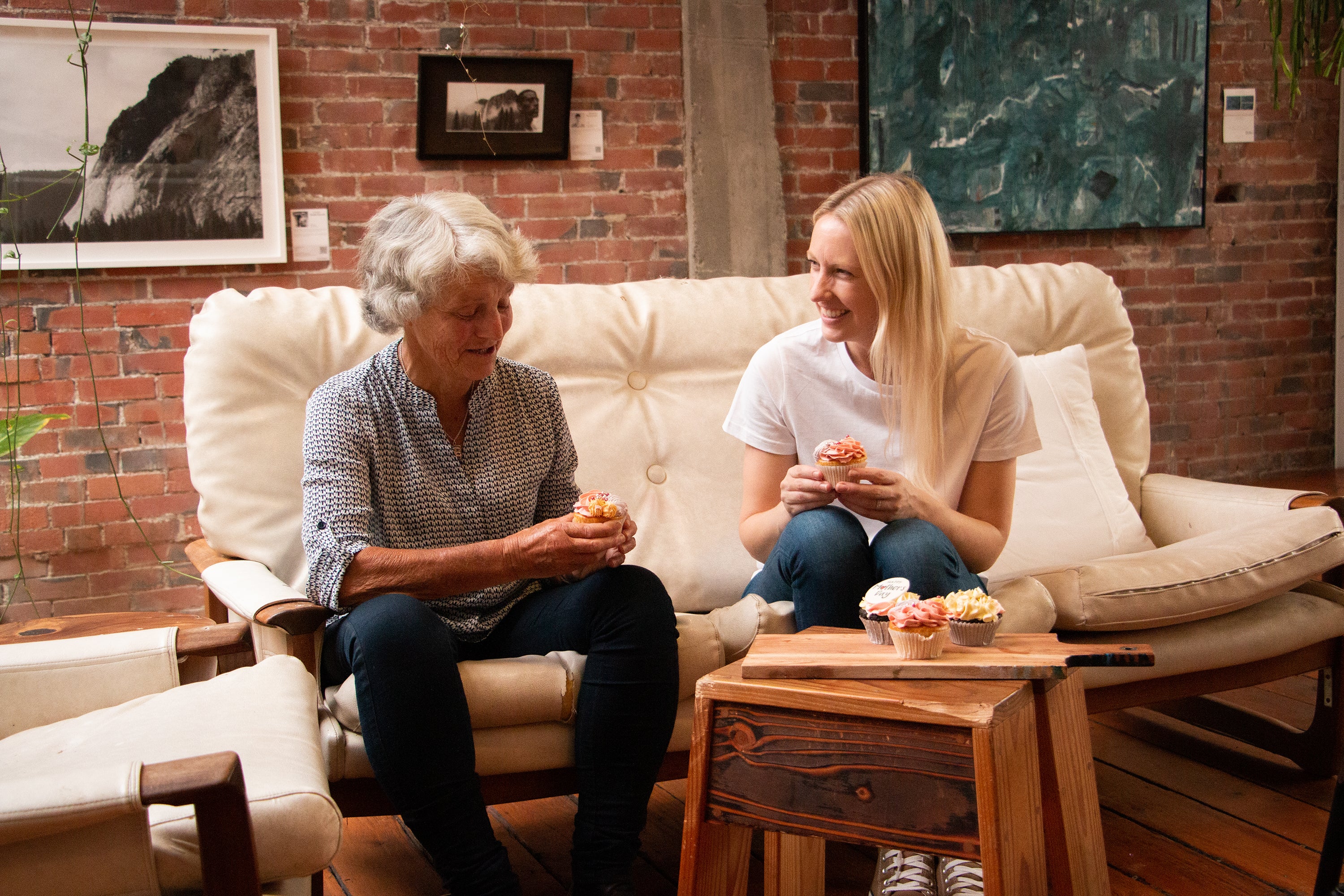 Mother and daughter sitting on the couch together chatting and sharing mother day cupcakes 